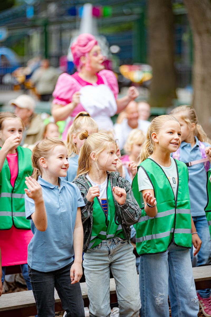 Kinderen in hesjes dansen mee met de show tijdens hun schoolreisje