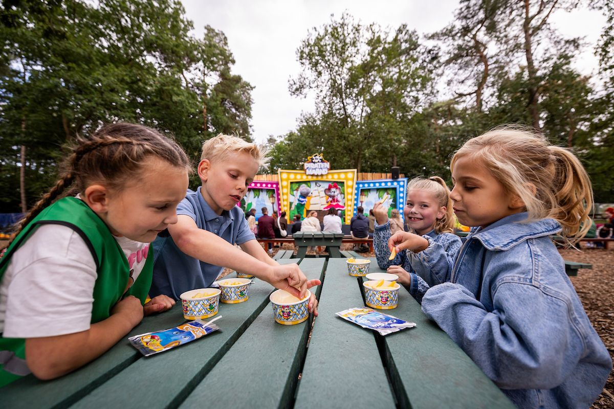 Kinderen eten frietjes aan de picknicktafel bij het podium